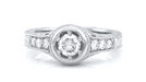 This White Gold Art Deco low profile ring setting for a 1/2 carat round diamond has a high polish halo circle around the center diamond and side diamonds on the top of the band - 3 stones on each side of the center diamond. Filigree under the setting and engraving down the sides of the ring is shown. R990W50NS