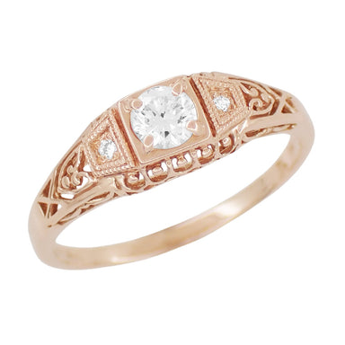 A rose gold filigree engagement ring with a central white sapphire and two side white sapphires set in a low-profile band.
