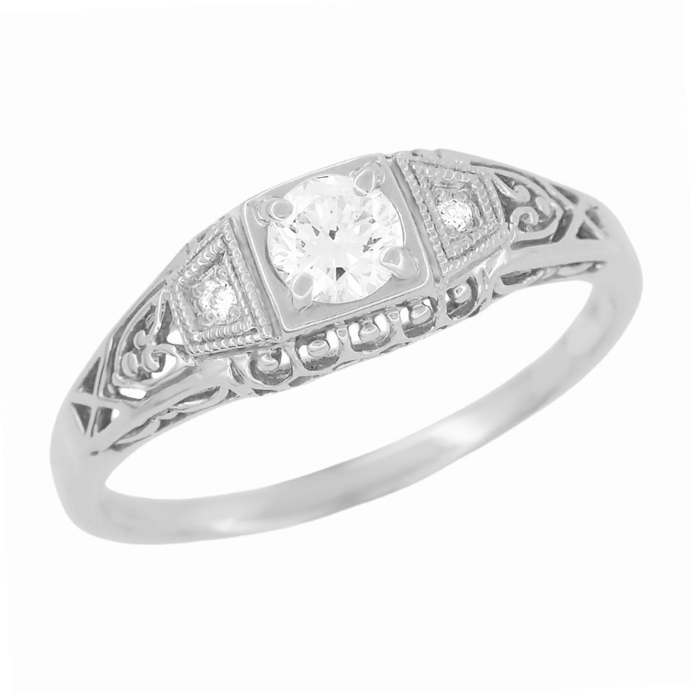 A 14 karat white gold engagement ring with a central white sapphire and two round white sapphire side stones, featuring Art Deco filigree detailing. R228WS