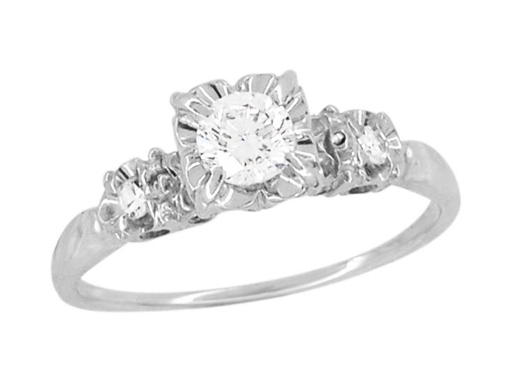 A white gold vintage three-stone diamond engagement ring with a round center diamond in an illusion box setting, and smaller diamonds on either side, set against a plain white background. R729