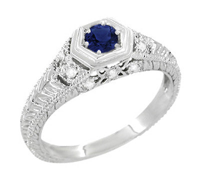 An Art Deco filigree sapphire engagement ring with a round brilliant cut natural royal blue sapphire center stone, in a hexagon frame, surrounded  by round brilliant cut diamonds on the sides, set in your choice of 14 karat or 10 karat white gold.